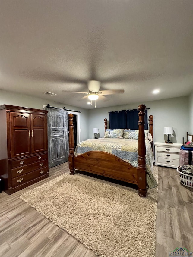 bedroom featuring ceiling fan, a barn door, a textured ceiling, and light wood-type flooring