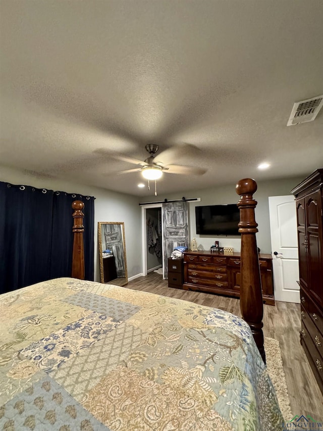 bedroom featuring ceiling fan, a barn door, light hardwood / wood-style floors, and a textured ceiling