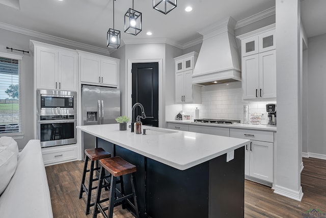 kitchen featuring sink, white cabinets, custom exhaust hood, stainless steel appliances, and a center island with sink