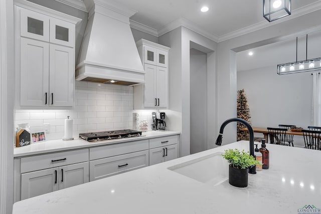 kitchen featuring premium range hood, decorative light fixtures, white cabinetry, sink, and light stone countertops