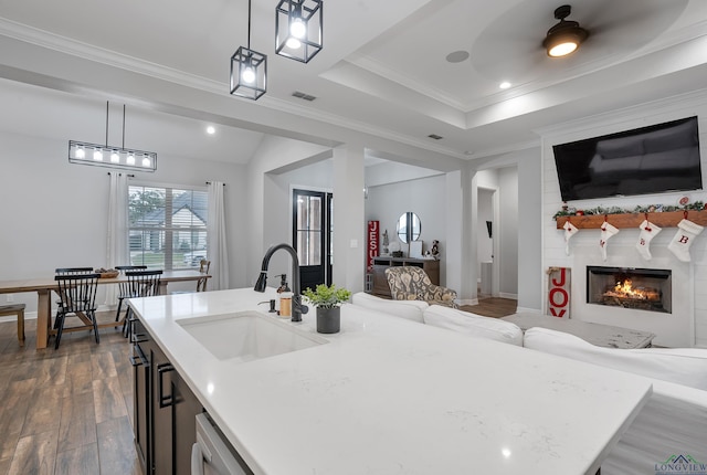 kitchen with sink, dark wood-type flooring, ornamental molding, a large fireplace, and decorative light fixtures