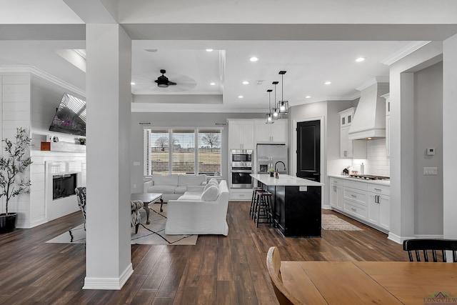 interior space with premium range hood, a kitchen bar, hanging light fixtures, a center island with sink, and stainless steel appliances