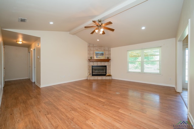 unfurnished living room featuring lofted ceiling with beams, ceiling fan, a tile fireplace, and light hardwood / wood-style flooring