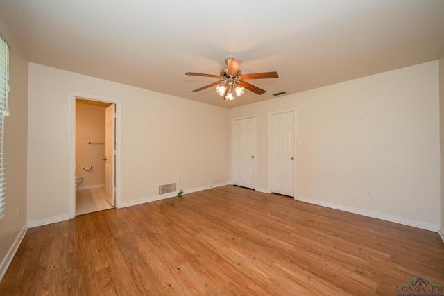 unfurnished bedroom featuring ceiling fan, two closets, light wood-type flooring, and ensuite bath