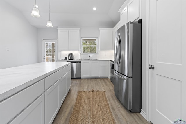 kitchen featuring white cabinetry, hanging light fixtures, stainless steel appliances, light hardwood / wood-style floors, and decorative backsplash