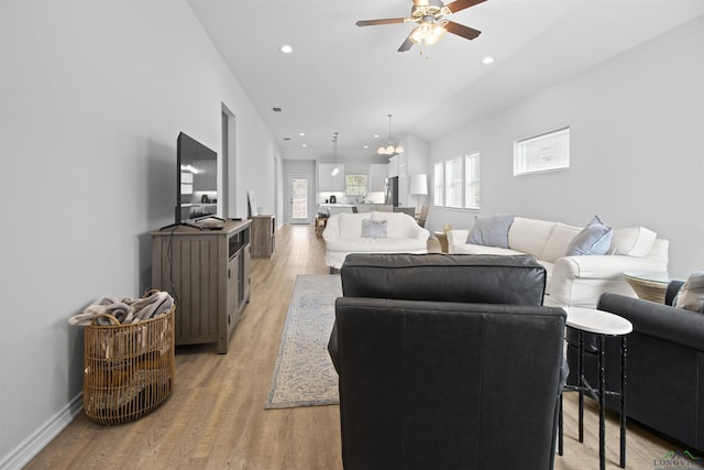 living room featuring ceiling fan with notable chandelier and light wood-type flooring