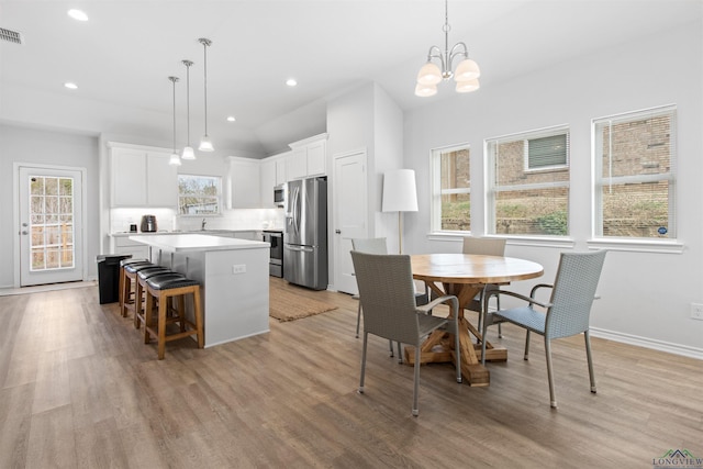 kitchen featuring white cabinetry, light wood-type flooring, appliances with stainless steel finishes, a kitchen island, and pendant lighting