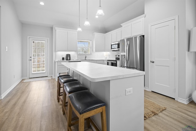 kitchen with a kitchen island, appliances with stainless steel finishes, a breakfast bar, white cabinets, and hanging light fixtures