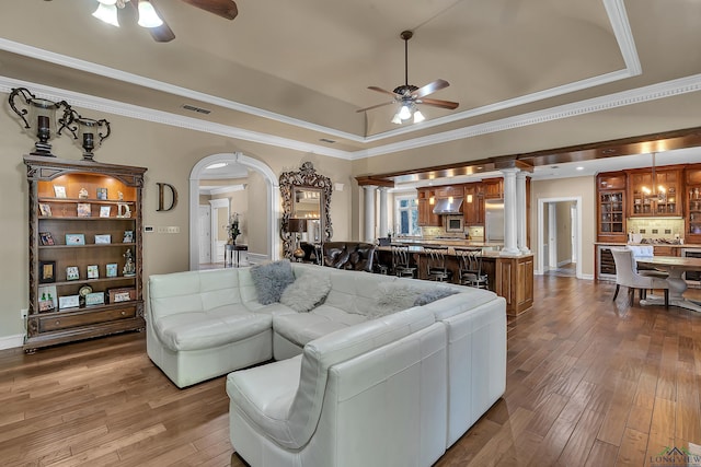 living room featuring ceiling fan, light hardwood / wood-style floors, decorative columns, and a tray ceiling