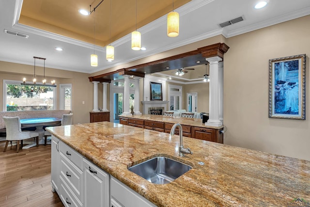 kitchen featuring light stone countertops, a tray ceiling, ornate columns, and white cabinets