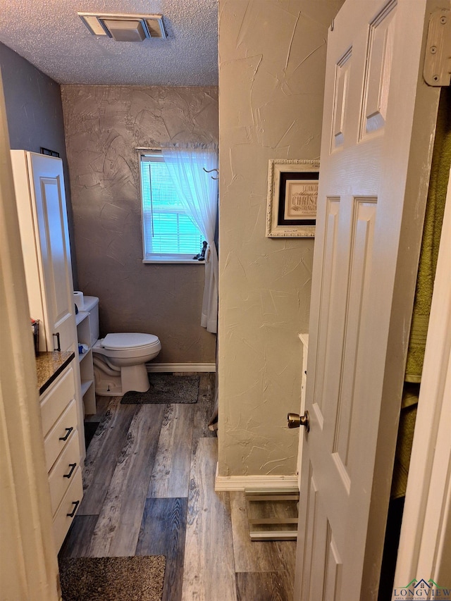 bathroom featuring vanity, wood-type flooring, toilet, and a textured ceiling