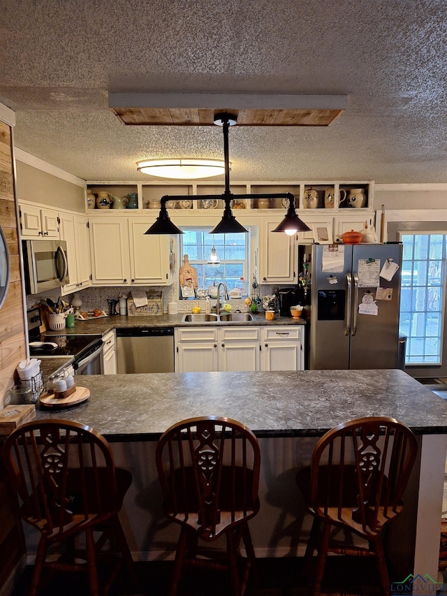 kitchen with a breakfast bar, sink, white cabinetry, appliances with stainless steel finishes, and kitchen peninsula