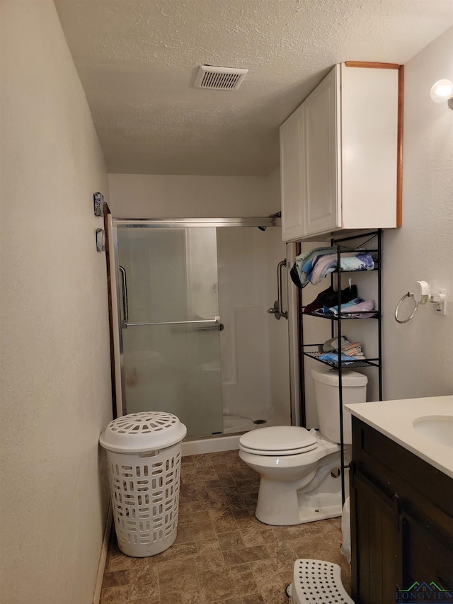 bathroom with a shower with door, vanity, a textured ceiling, and toilet