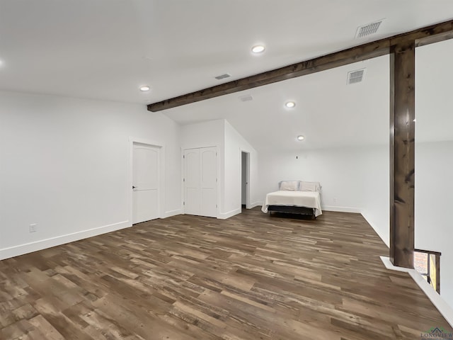 unfurnished bedroom with a barn door, dark hardwood / wood-style floors, and vaulted ceiling with beams