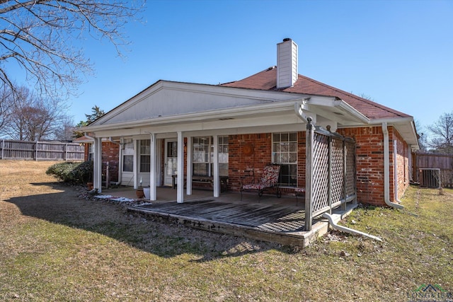 back of property with a yard, brick siding, a chimney, and fence