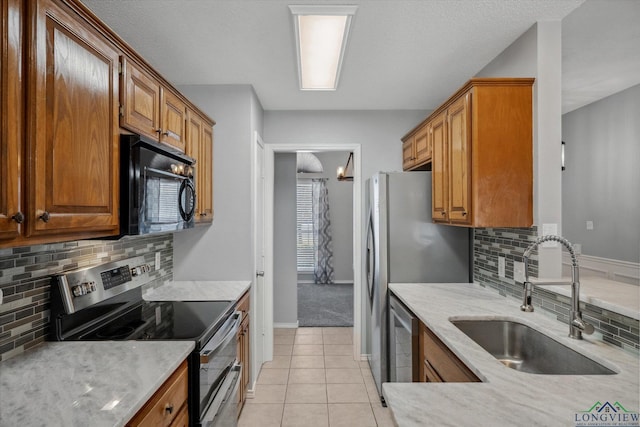 kitchen with light tile patterned flooring, a sink, appliances with stainless steel finishes, brown cabinets, and tasteful backsplash