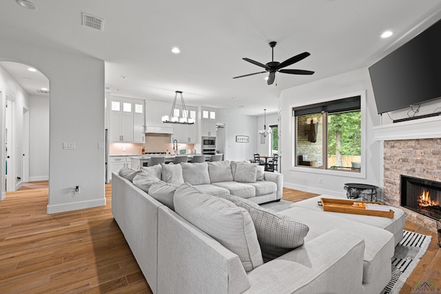 living room featuring a stone fireplace, ceiling fan with notable chandelier, and light wood-type flooring