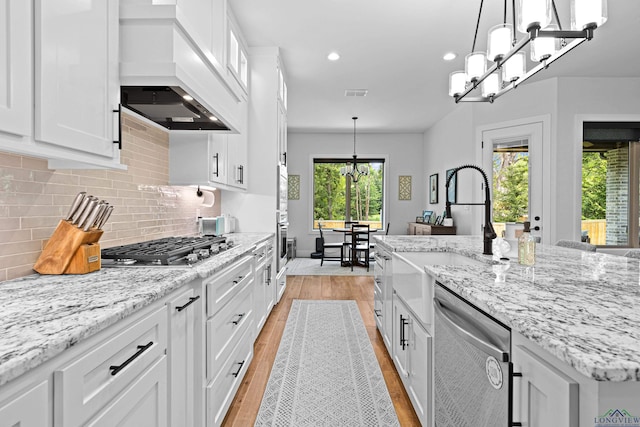 kitchen featuring custom exhaust hood, stainless steel appliances, a kitchen island with sink, decorative light fixtures, and white cabinets