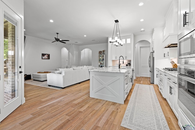 kitchen featuring backsplash, a kitchen island with sink, white cabinets, decorative light fixtures, and stainless steel appliances