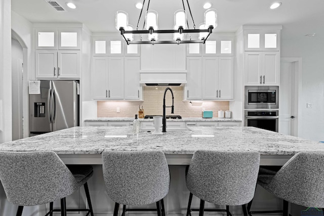 kitchen featuring decorative backsplash, a large island with sink, stainless steel appliances, and white cabinetry