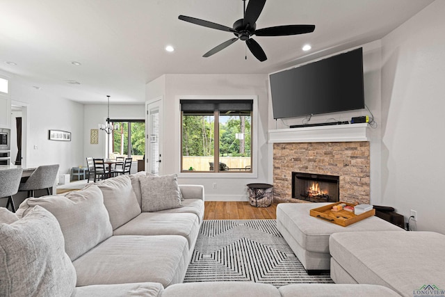 living room with a stone fireplace, ceiling fan with notable chandelier, and hardwood / wood-style flooring