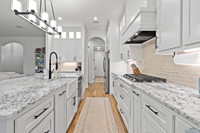 kitchen with white cabinetry, light stone counters, pendant lighting, custom range hood, and appliances with stainless steel finishes