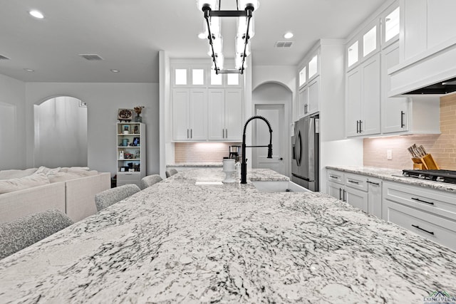 kitchen with white cabinets, decorative backsplash, light stone countertops, and stainless steel appliances