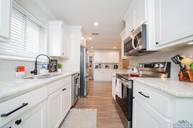 kitchen with appliances with stainless steel finishes, white cabinetry, sink, light stone countertops, and light hardwood / wood-style flooring