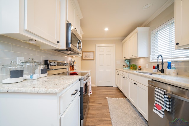 kitchen featuring appliances with stainless steel finishes, white cabinetry, sink, ornamental molding, and light stone counters