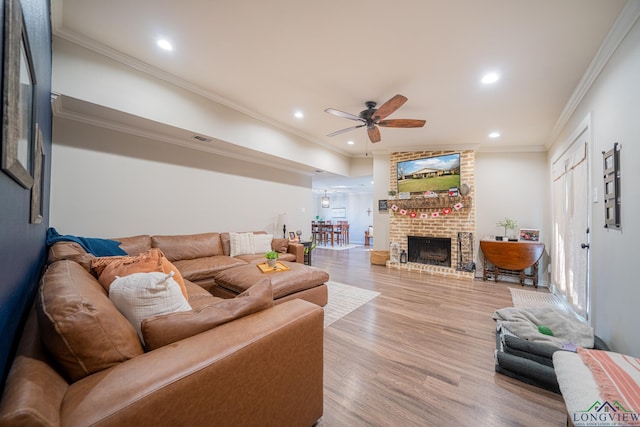 living room featuring crown molding, ceiling fan, a fireplace, and light hardwood / wood-style floors