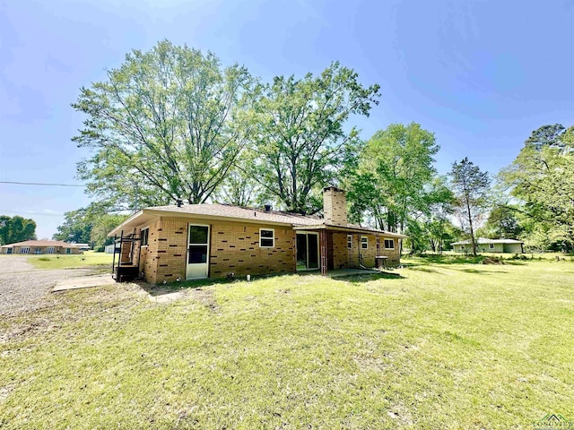 back of house with brick siding, a lawn, and a chimney