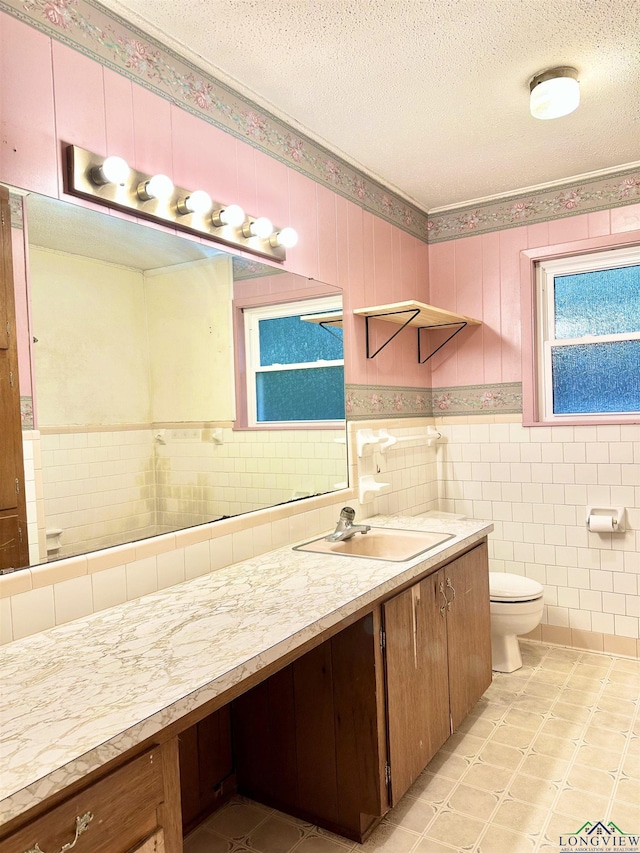 bathroom featuring tile walls, toilet, a textured ceiling, vanity, and wainscoting
