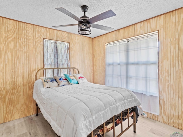 bedroom with ceiling fan, light wood-type flooring, wooden walls, and a textured ceiling