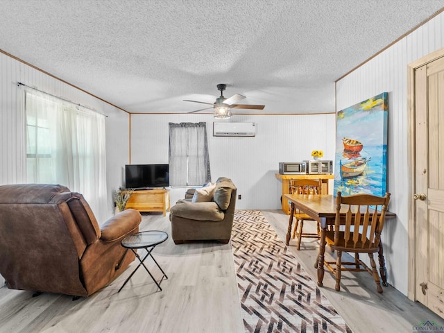 living room featuring ceiling fan, a wall mounted air conditioner, light wood-type flooring, a textured ceiling, and ornamental molding