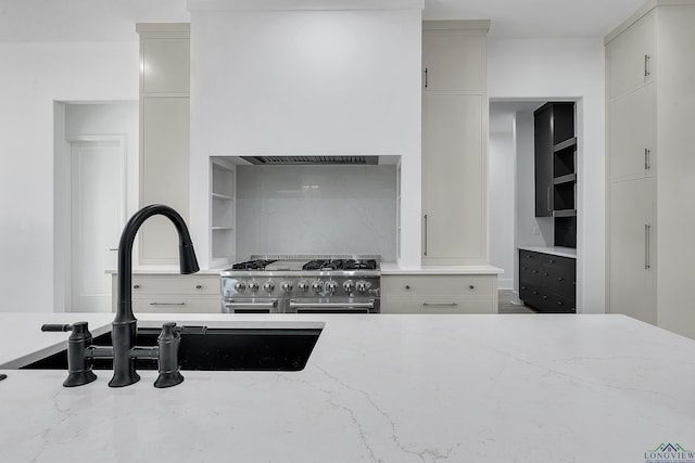 kitchen with sink, decorative backsplash, double oven range, light stone counters, and wall chimney range hood