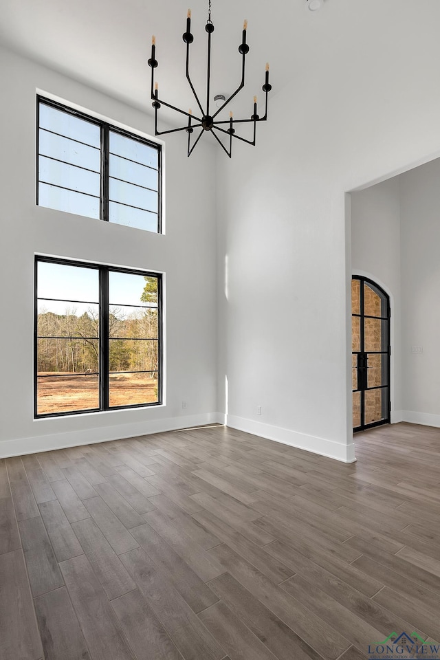 unfurnished living room featuring a high ceiling, wood-type flooring, and a chandelier