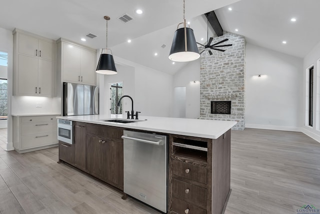 kitchen with pendant lighting, sink, appliances with stainless steel finishes, light hardwood / wood-style floors, and a center island with sink