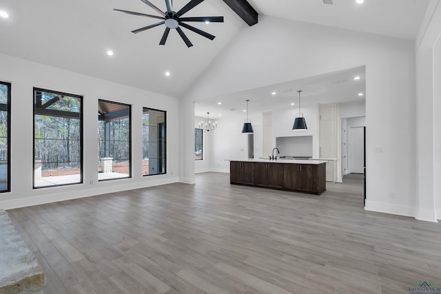 unfurnished living room with sink, high vaulted ceiling, hardwood / wood-style floors, beamed ceiling, and ceiling fan with notable chandelier