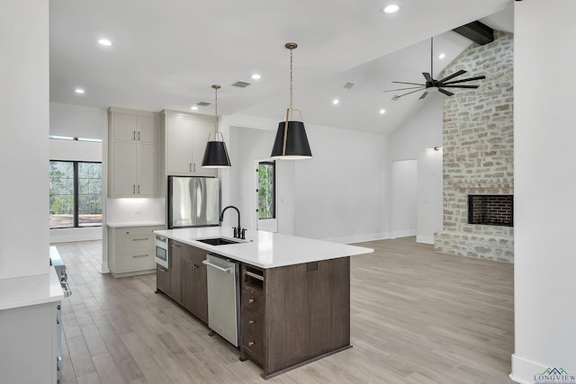 kitchen with sink, a center island with sink, stainless steel appliances, a fireplace, and light hardwood / wood-style floors