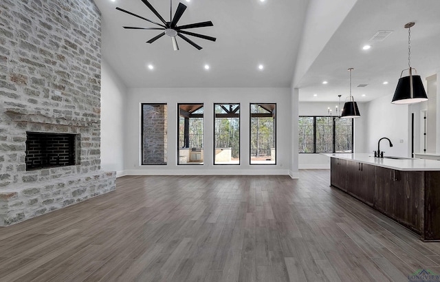 unfurnished living room with sink, ceiling fan, high vaulted ceiling, a large fireplace, and dark hardwood / wood-style flooring