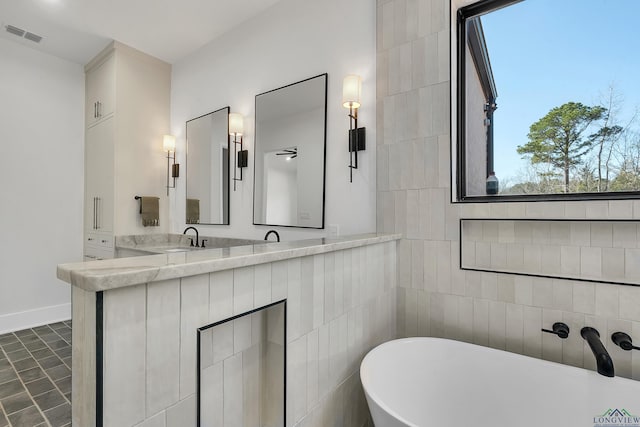 bathroom with a healthy amount of sunlight, a bathtub, vanity, and tile walls