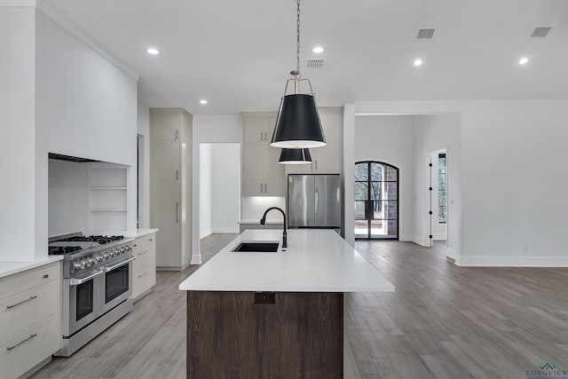 kitchen with appliances with stainless steel finishes, an island with sink, sink, hanging light fixtures, and light hardwood / wood-style flooring