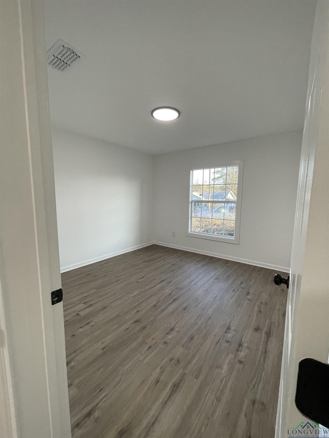 unfurnished room with dark wood-style flooring, visible vents, and baseboards