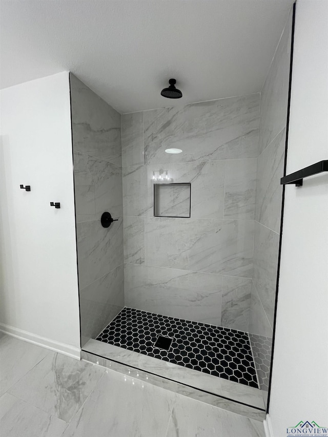 bathroom with marble finish floor, a tile shower, and baseboards