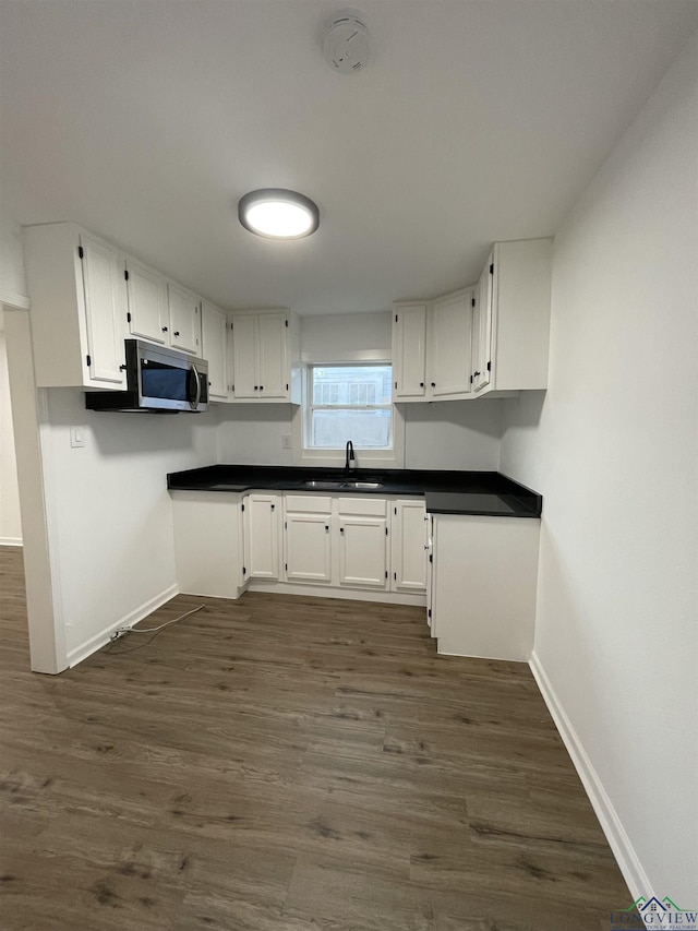 kitchen with dark wood finished floors, white cabinets, stainless steel microwave, and a sink