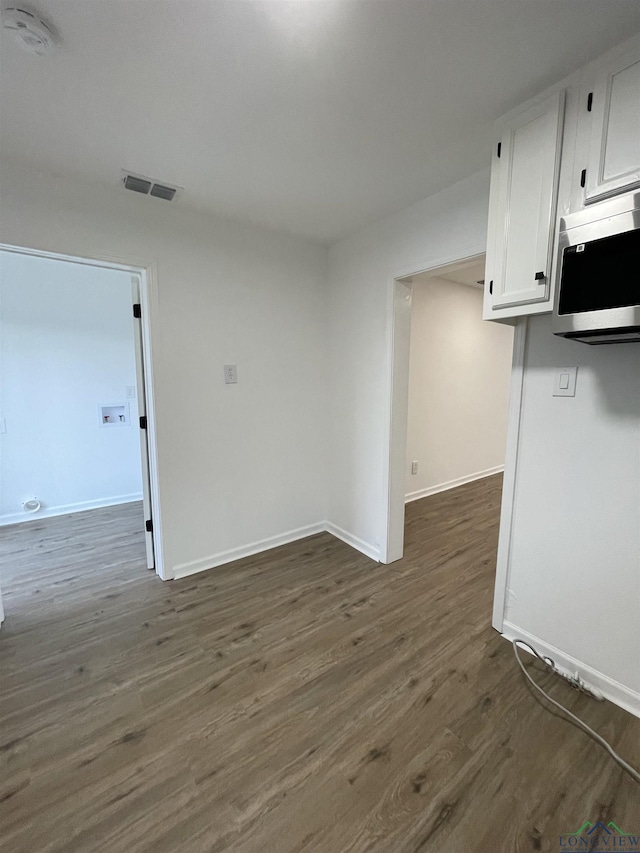 empty room featuring dark wood-style flooring, visible vents, and baseboards