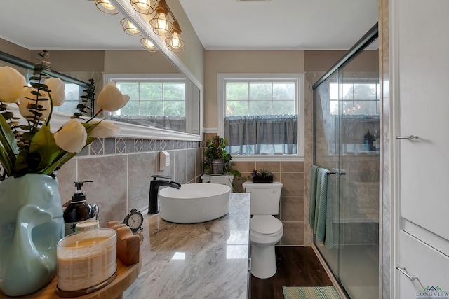 bathroom with a shower with shower door, sink, toilet, tile walls, and wood-type flooring