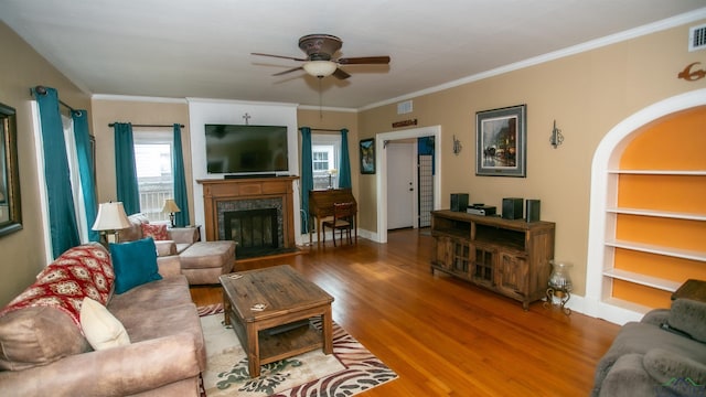 living room featuring wood finished floors, a ceiling fan, crown molding, and a fireplace with raised hearth