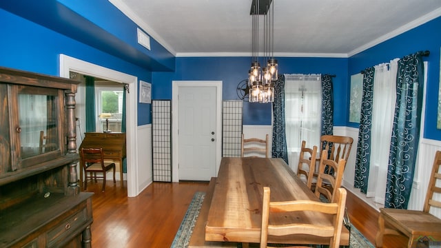 dining area with a chandelier, wainscoting, wood finished floors, and crown molding