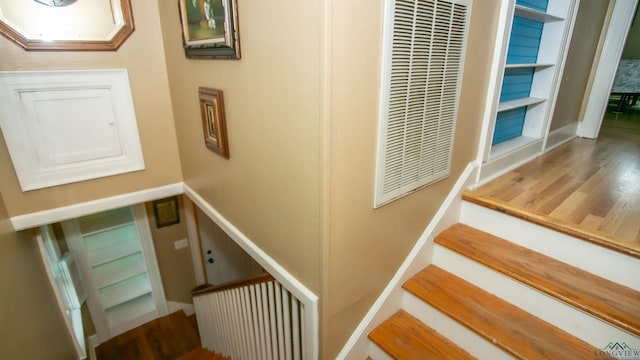stairway with a heating unit, wood finished floors, and baseboards